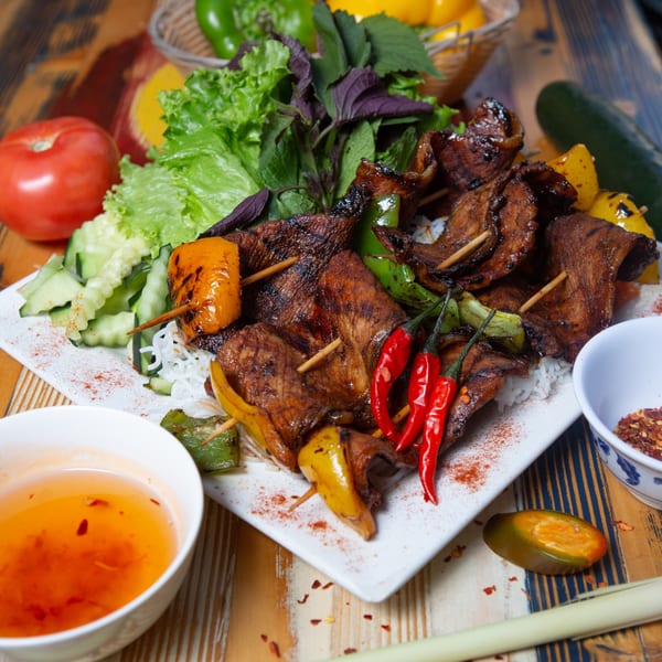 Grilled pork skewers with bell peppers, fresh herbs, and chili on a bed of vermicelli noodles.