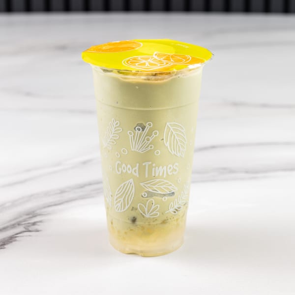 A green smoothie in a clear cup with a yellow lid, on a white marble surface.