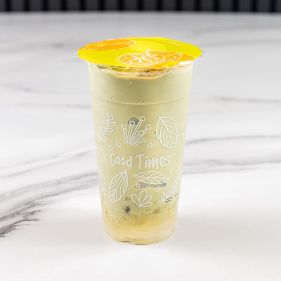 A green smoothie in a clear cup with a yellow lid, on a white marble surface.