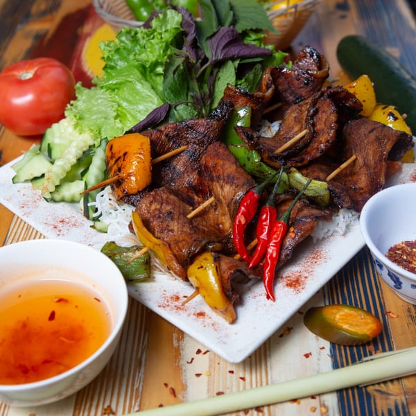 Vietnamese grilled pork skewers with bell peppers, fresh herbs, rice noodles, and dipping sauce.