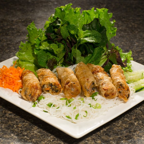 Vietnamese fried spring rolls with vermicelli noodles, shredded carrots, cucumber, lettuce, and mint on a plate.