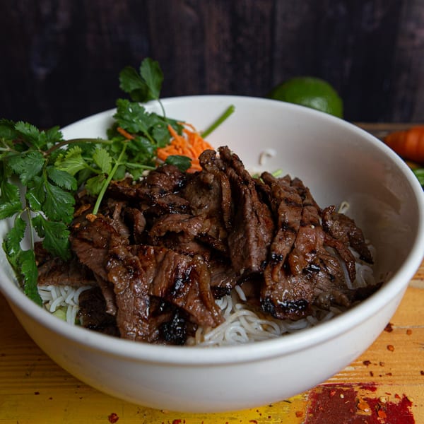 A white bowl of Phở 95's Vietnamese grilled beef vermicelli with cilantro and shredded carrots.