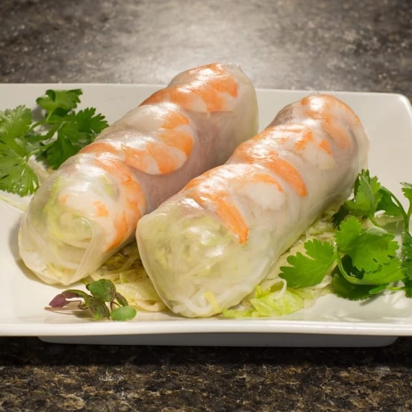 Two fresh Vietnamese spring rolls with shrimp, lettuce, and herbs on a white rectangular plate.