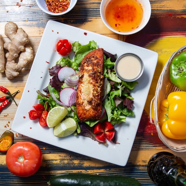 Crispy salmon with fresh salad, lime, radish, and cherry tomatoes, surrounded by spices and vegetables.