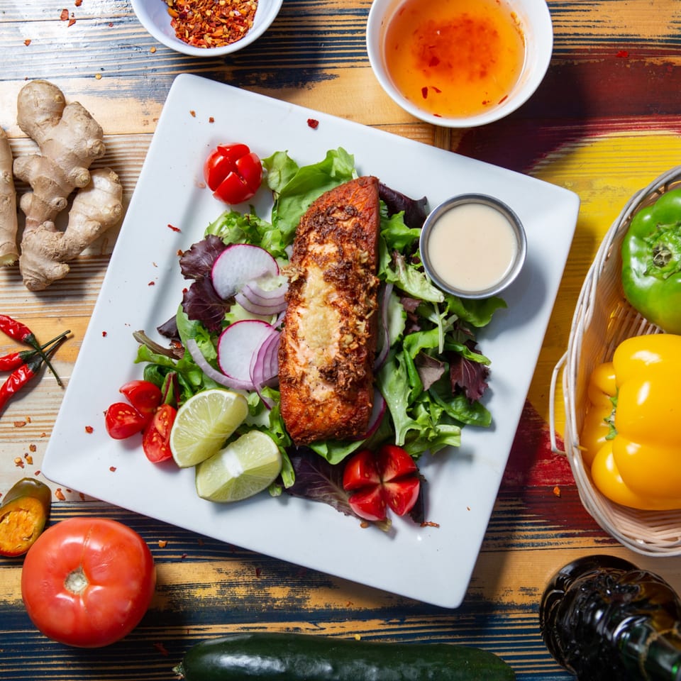 Crispy salmon with fresh salad, lime, radish, and cherry tomatoes, surrounded by spices and vegetables.