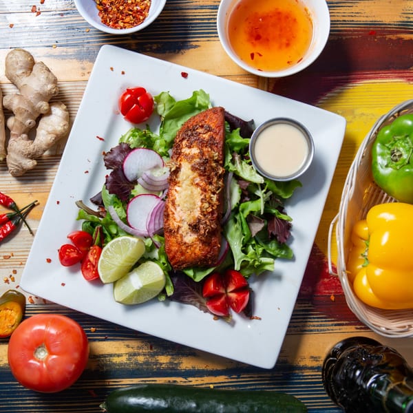 Grilled salmon with salad, lime, and tomatoes, served with sauce on a colorful wooden table.