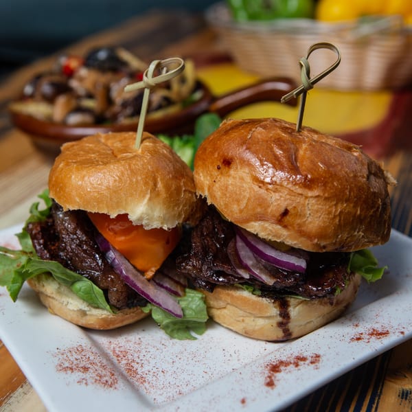 Two Vietnamese sliders with beef, red onion, and lettuce on a white plate.