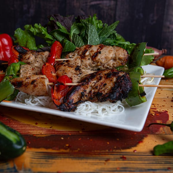 Grilled chicken and bell pepper skewers on a bed of vermicelli noodles with fresh herbs.