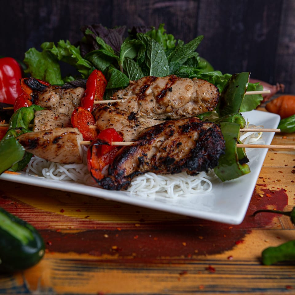 Grilled chicken and bell pepper skewers on a bed of vermicelli noodles with fresh herbs.