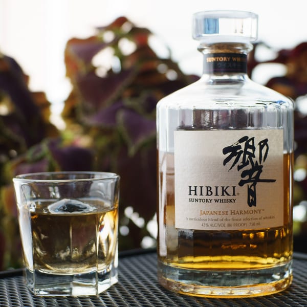 A bottle of Hibiki Suntory Whisky and a glass with ice and whisky on a metal grate.